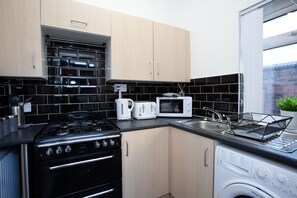 A modern kitchen with a gas stove, white appliances, and a built-in washing machine. - Salford House (Salford)