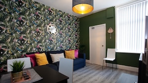 A modern living room with a patterned wallpaper, a blue sofa, a white chair, and a dining area with a table and chairs. - Salford House (Salford)