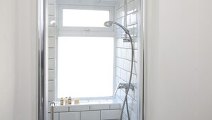A bathroom with a shower, a window, and toiletries on the windowsill. - Salford House (Salford)
