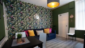 A modern living room with a tropical wallpaper, a dark blue sofa, and a white chair. - Salford House (Salford)