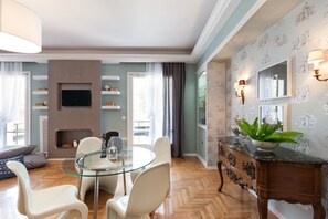 Uma sala de estar moderna com uma mesa de jantar de vidro, cadeiras brancas, lareira e um espelho decorativo.