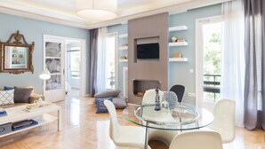 A modern living room with a glass coffee table, white chairs, a fireplace, and a TV mounted on the wall. - Acropoli's Luxury Apartment (Athens)