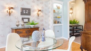 A dining area with a glass table, white chairs, a wooden cabinet, and wall-mounted sconces. - Acropoli's Luxury Apartment (Athens)