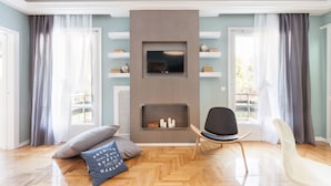 A modern living room with a flat-screen TV mounted on a wall, wooden flooring, and a seating area with two chairs. - Acropoli's Luxury Apartment (Athens)