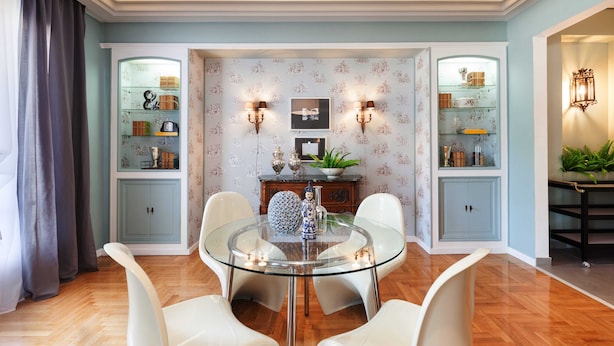 A dining area with a glass table surrounded by white chairs, flanked by two glass-fronted cabinets with shelves. - Acropoli's Luxury Apartment (Athens)