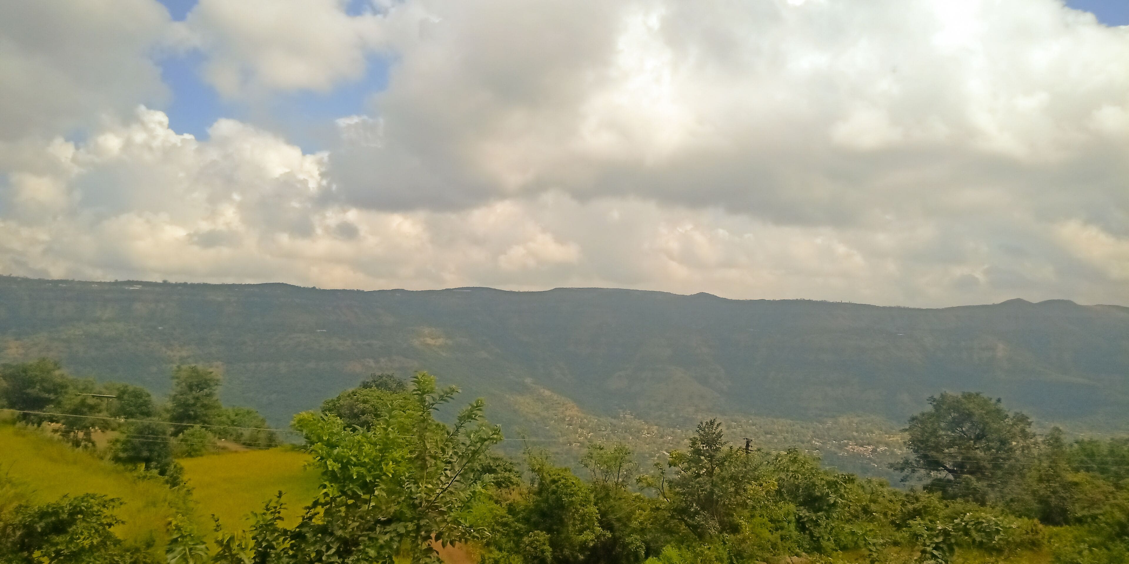 Un paysage montagneux avec une vallée et quelques arbres dispersés.