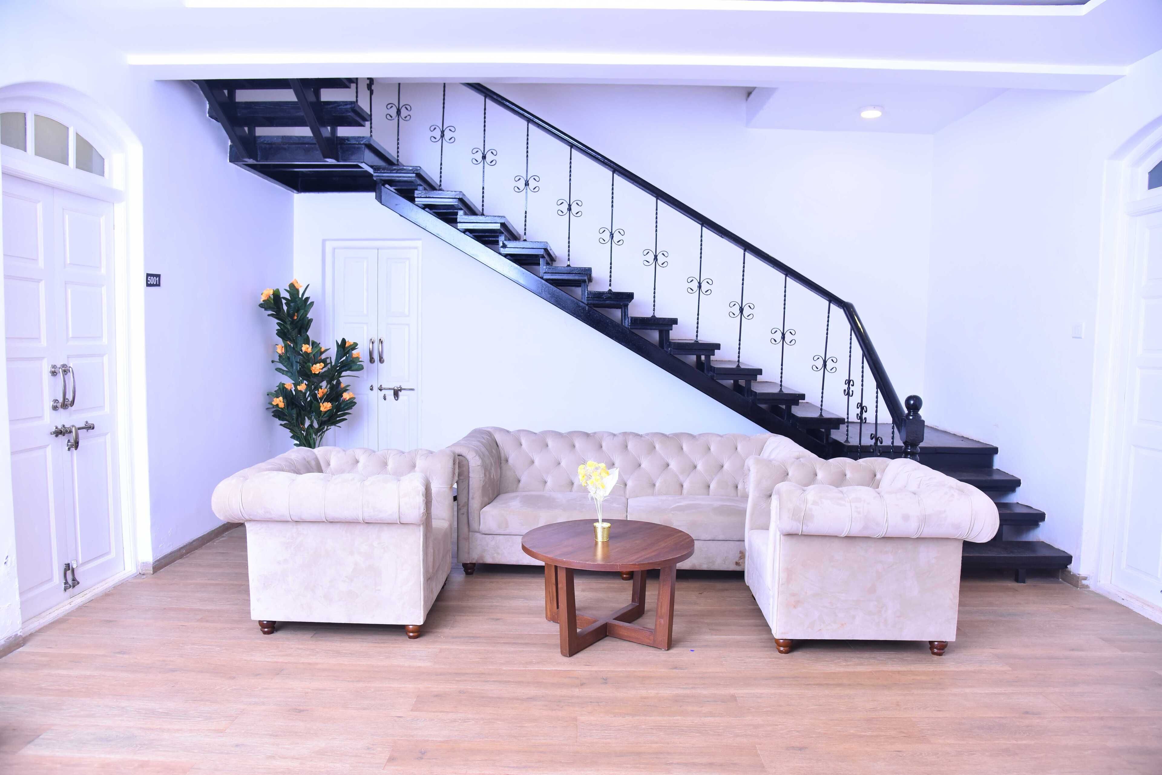 Una sala de estar con un sofá seccional color beige, una mesa de centro redonda de madera y una escalera con barandillas negras.