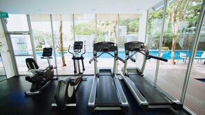 Une salle de sport équipée de tapis de course, de vélos d’appartement et d’un appareil d’aviron, avec de grandes fenêtres et une vue sur une piscine à l’extérieur.