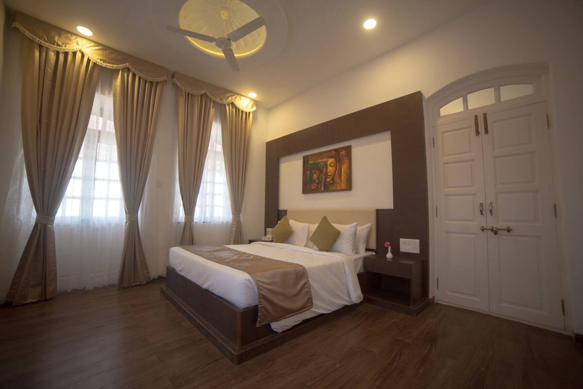 A hotel room with a large bed, a ceiling fan, a painting on the wall, and a wardrobe.