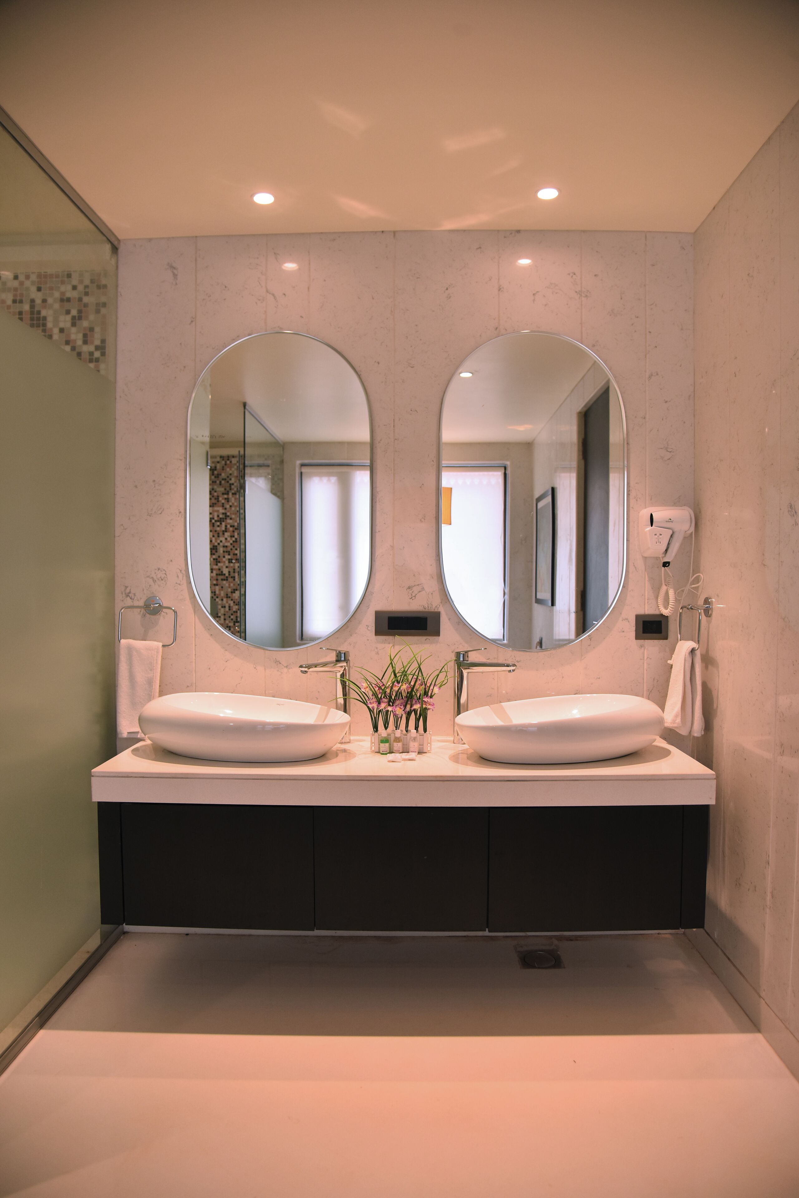 A modern bathroom with a double vanity, two round mirrors, and a built-in hairdryer.