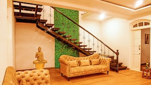 Un salon avec un escalier en bois, un mur vert, une statue de Bouddha et un canapé beige.