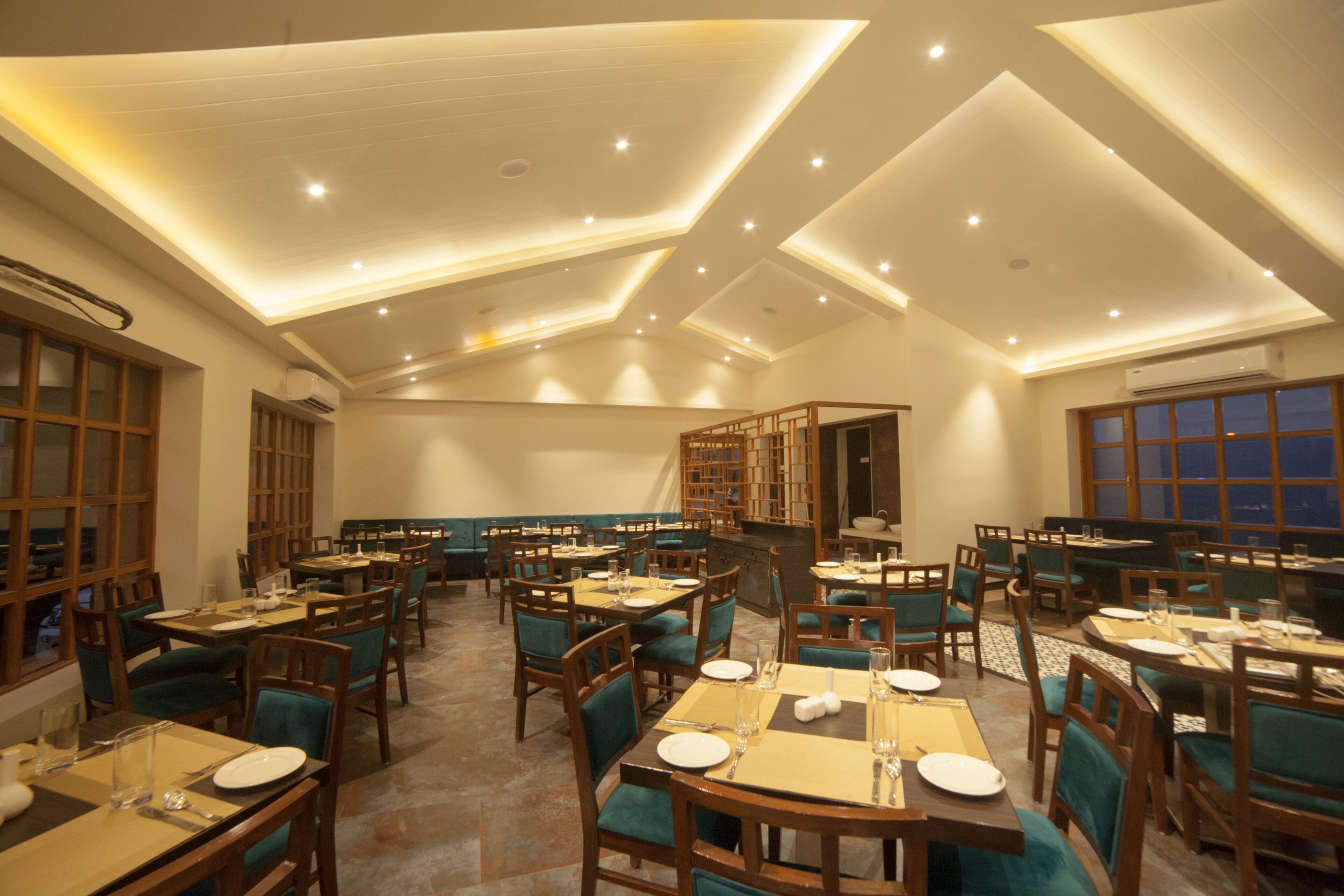 A spacious dining area with multiple tables and chairs, recessed ceiling lighting, and large windows.