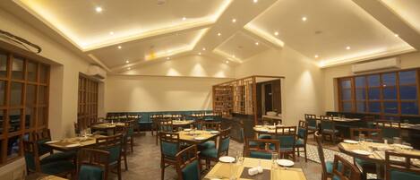 A spacious dining area with multiple tables and chairs, recessed ceiling lighting, and large windows.