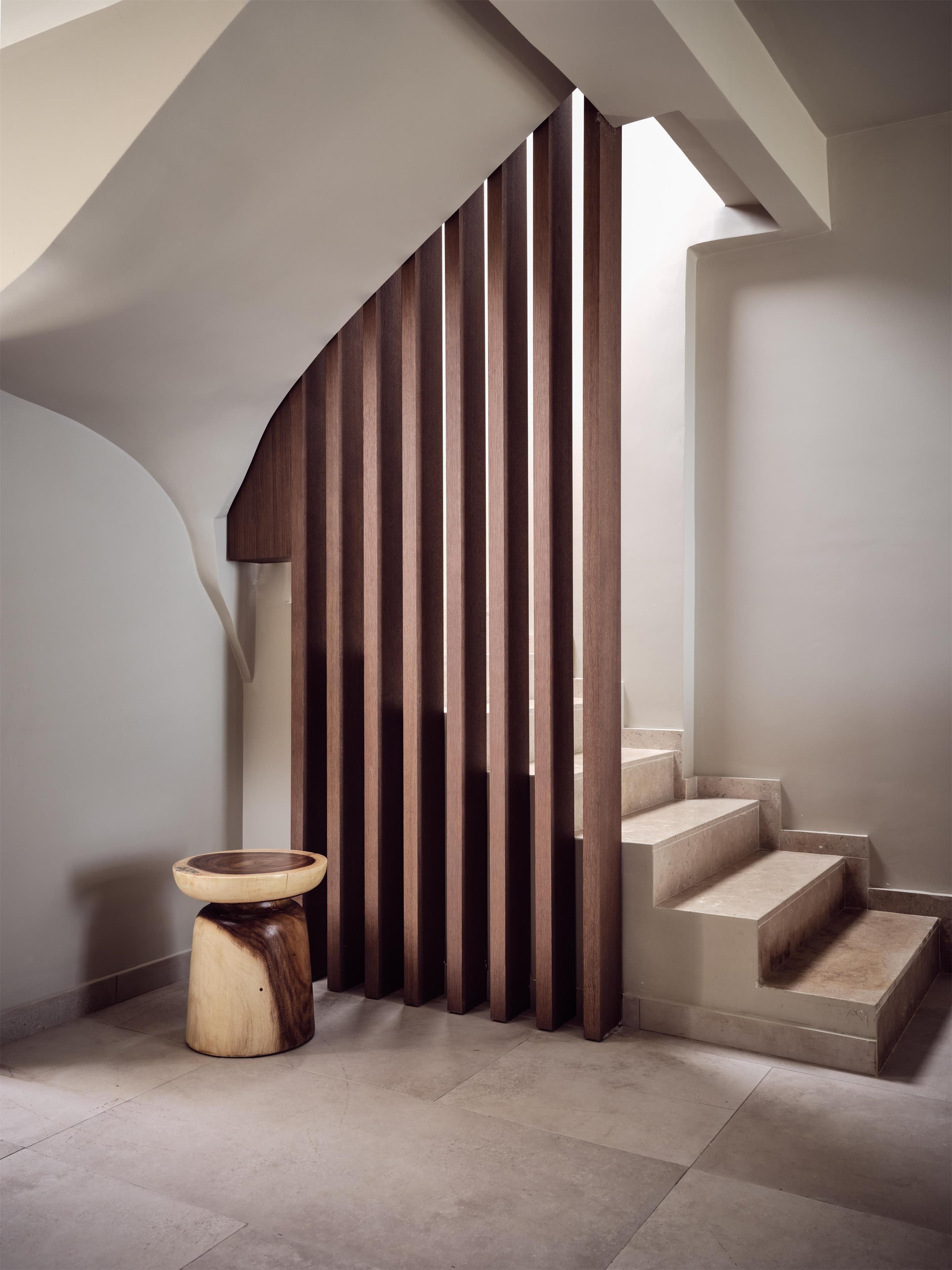 A modern interior with a wooden slatted wall, a round wooden stool, and a staircase.