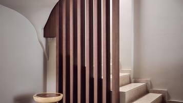 A modern interior with a wooden slatted wall, a round wooden stool, and a staircase.