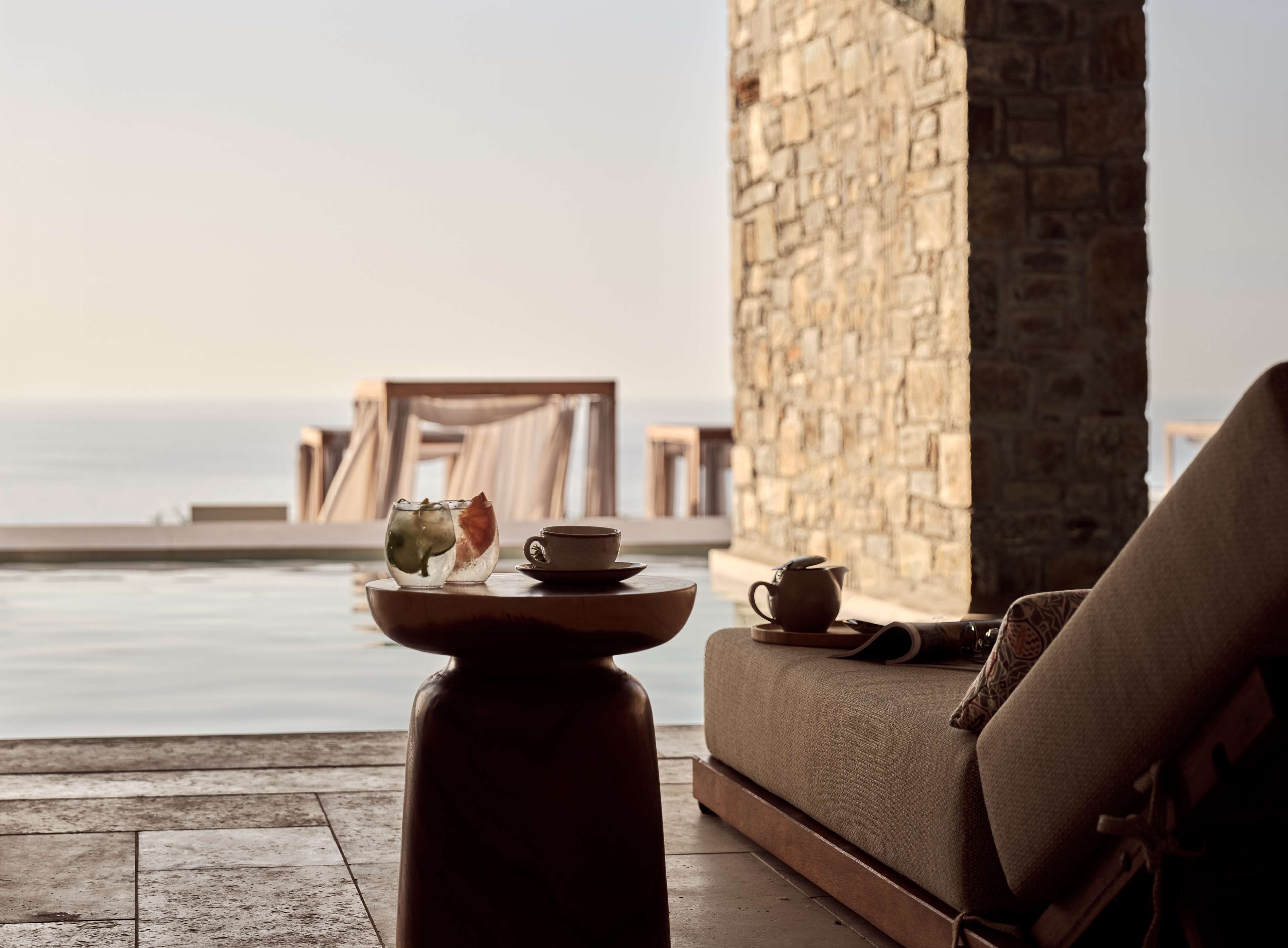 A serene outdoor seating area with a stone wall and a view of the sea.