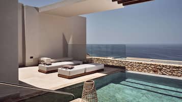 Una piscina infinita moderna con agua cristalina, una pared de piedra y un área de descanso con sofás y cojines blancos.