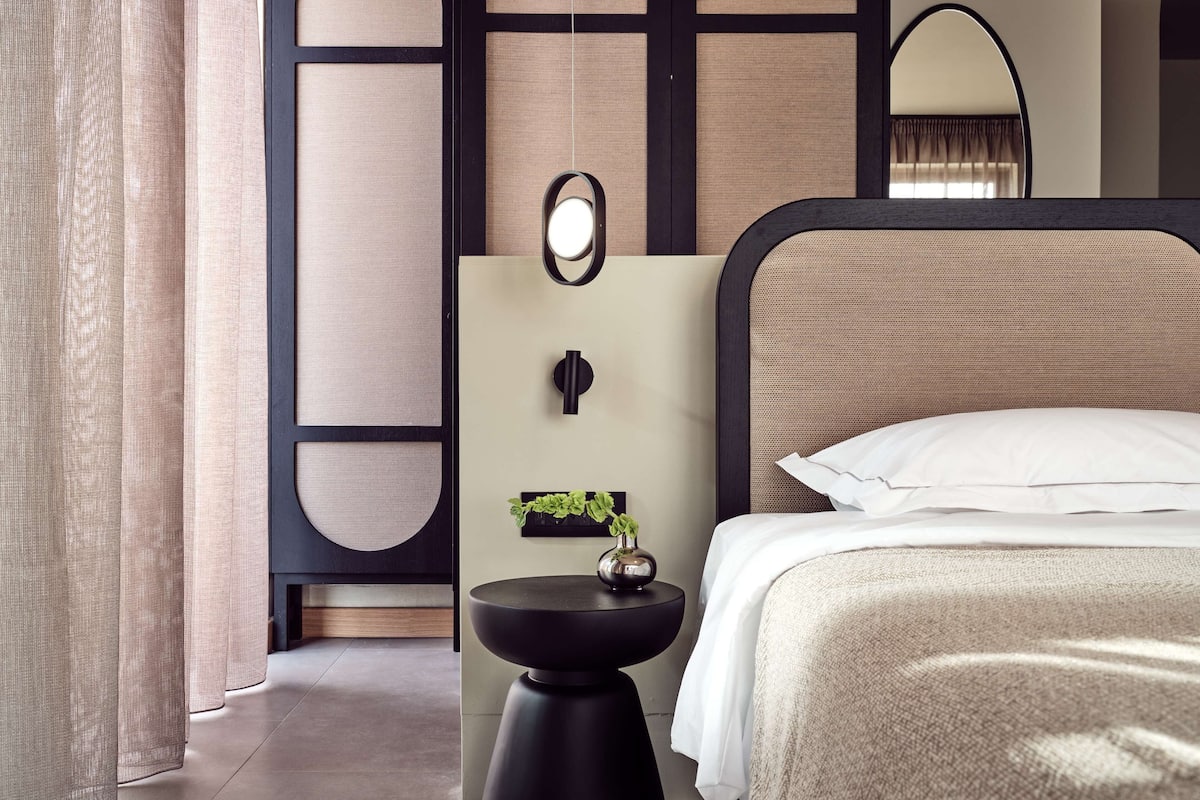 Un dormitorio moderno con una cama, una mesita de noche con una planta y un espejo montado en la pared.