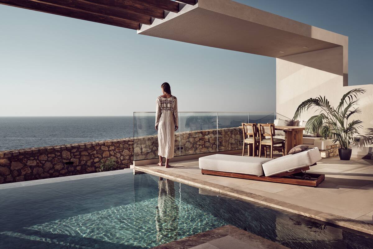 Una mujer de pie junto a una piscina con vista al mar.