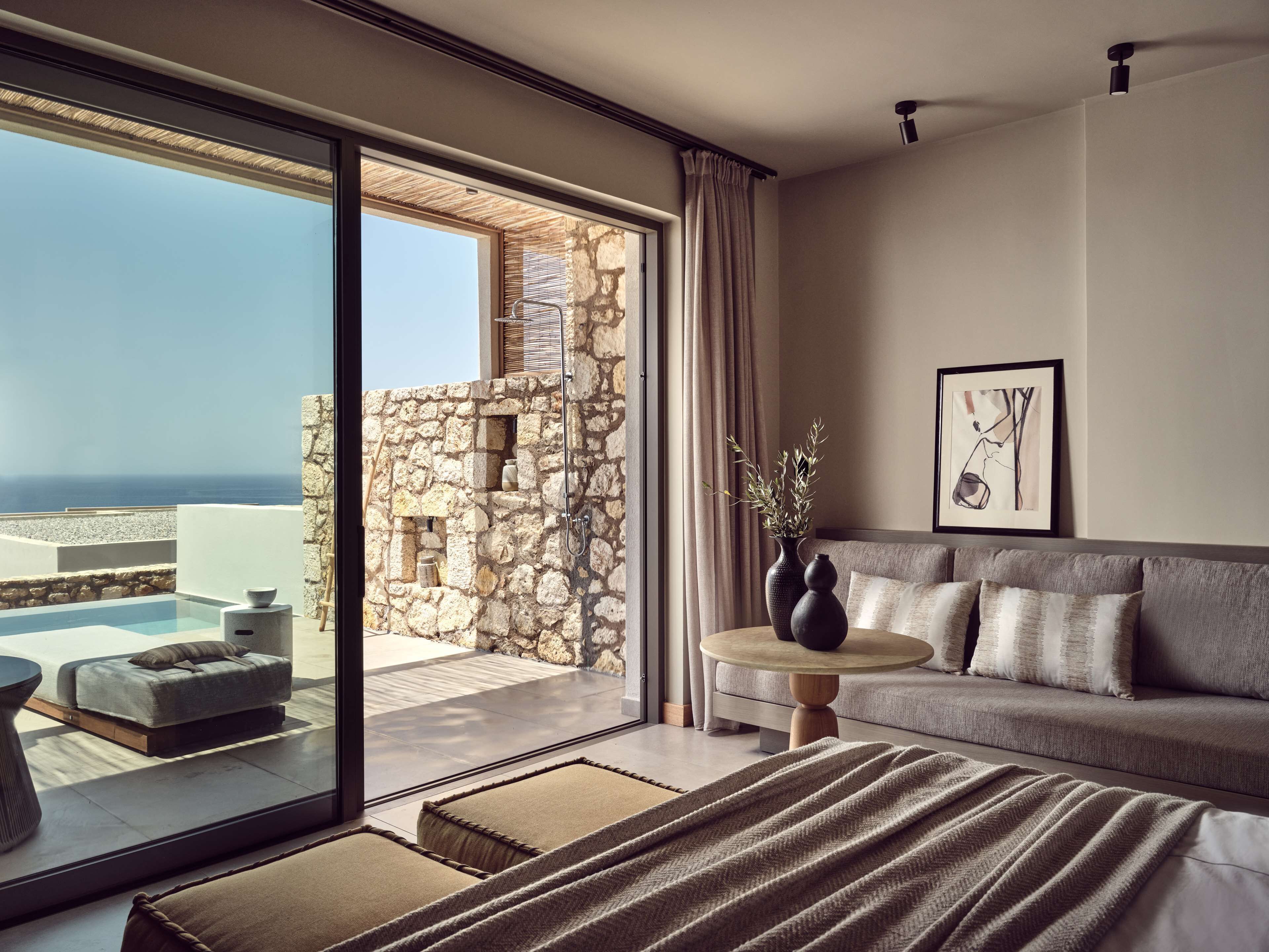 Un dormitorio moderno con un gran ventanal que da a un balcón con pared de piedra y vistas al mar.