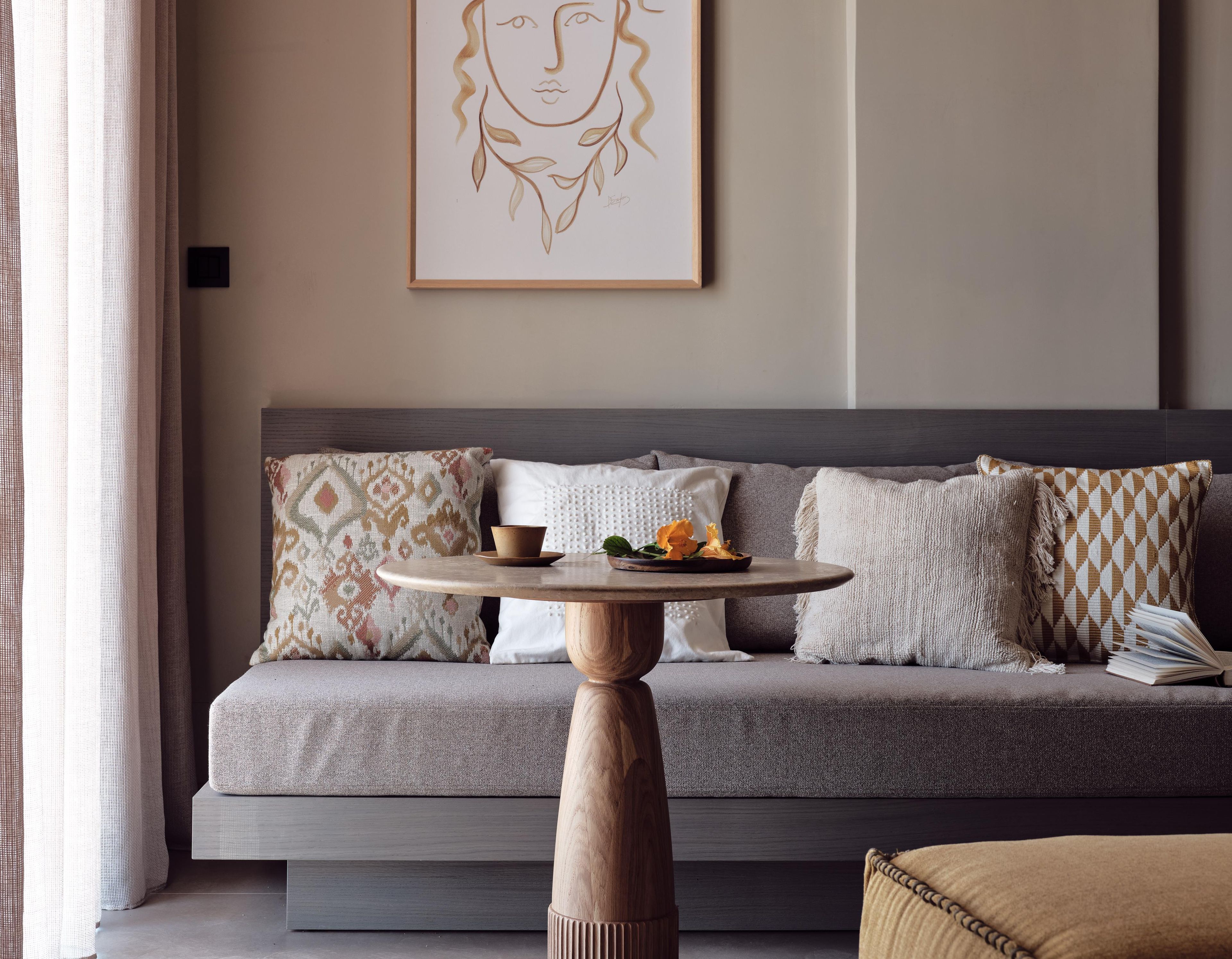 A modern living room with a grey sofa, patterned cushions, a wooden coffee table, and a framed artwork on the wall.