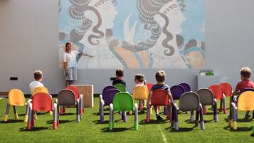 A classroom with children seated on colorful chairs facing a presentation.