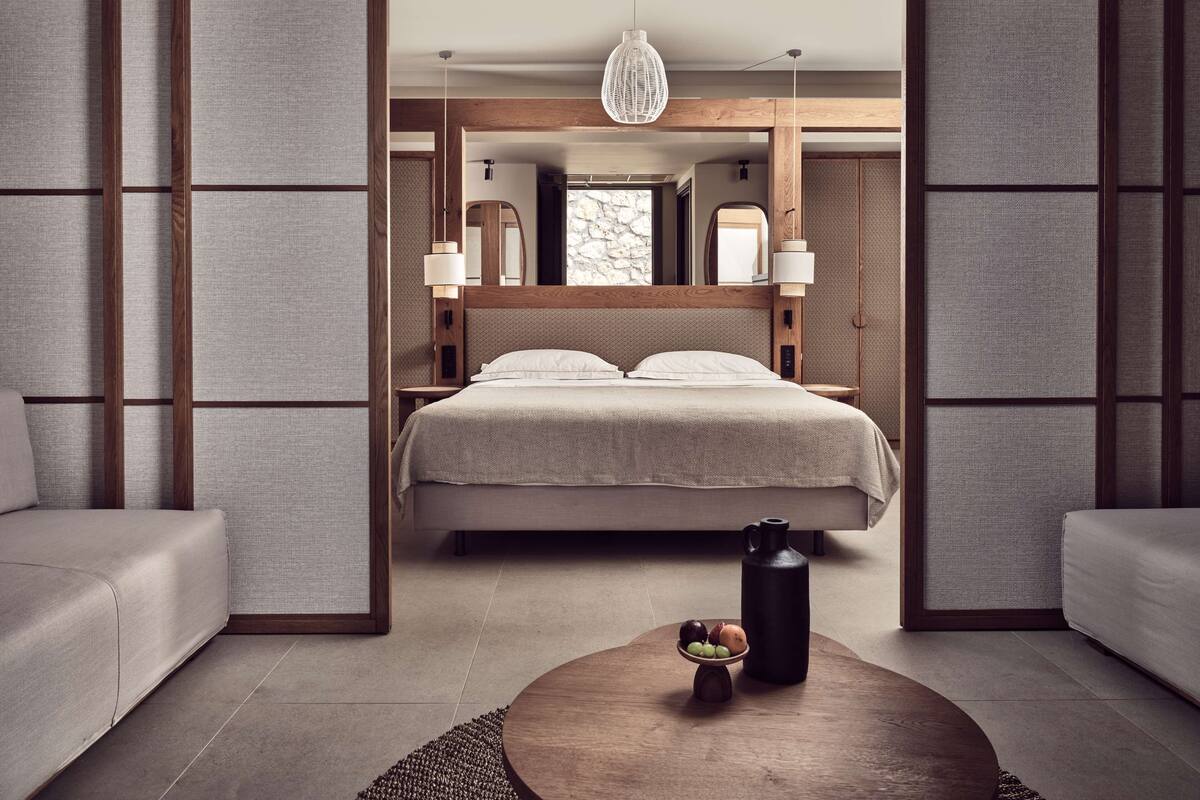 Un dormitorio moderno con cama, mesitas de noche, lámpara colgante y una mesa de centro con frutas.