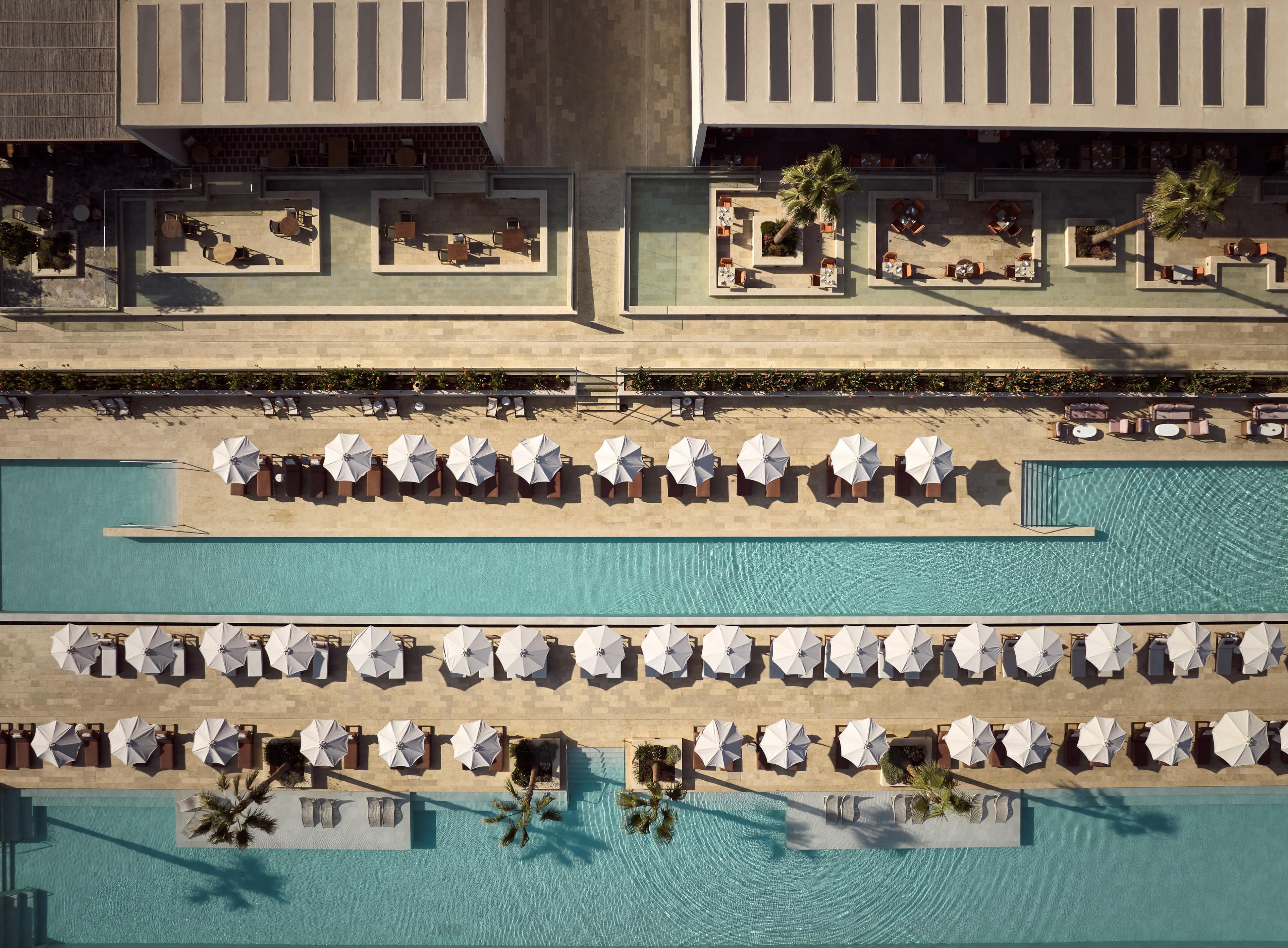 A rooftop pool area with multiple levels of seating and sun loungers, surrounded by a building with a modern architectural design.