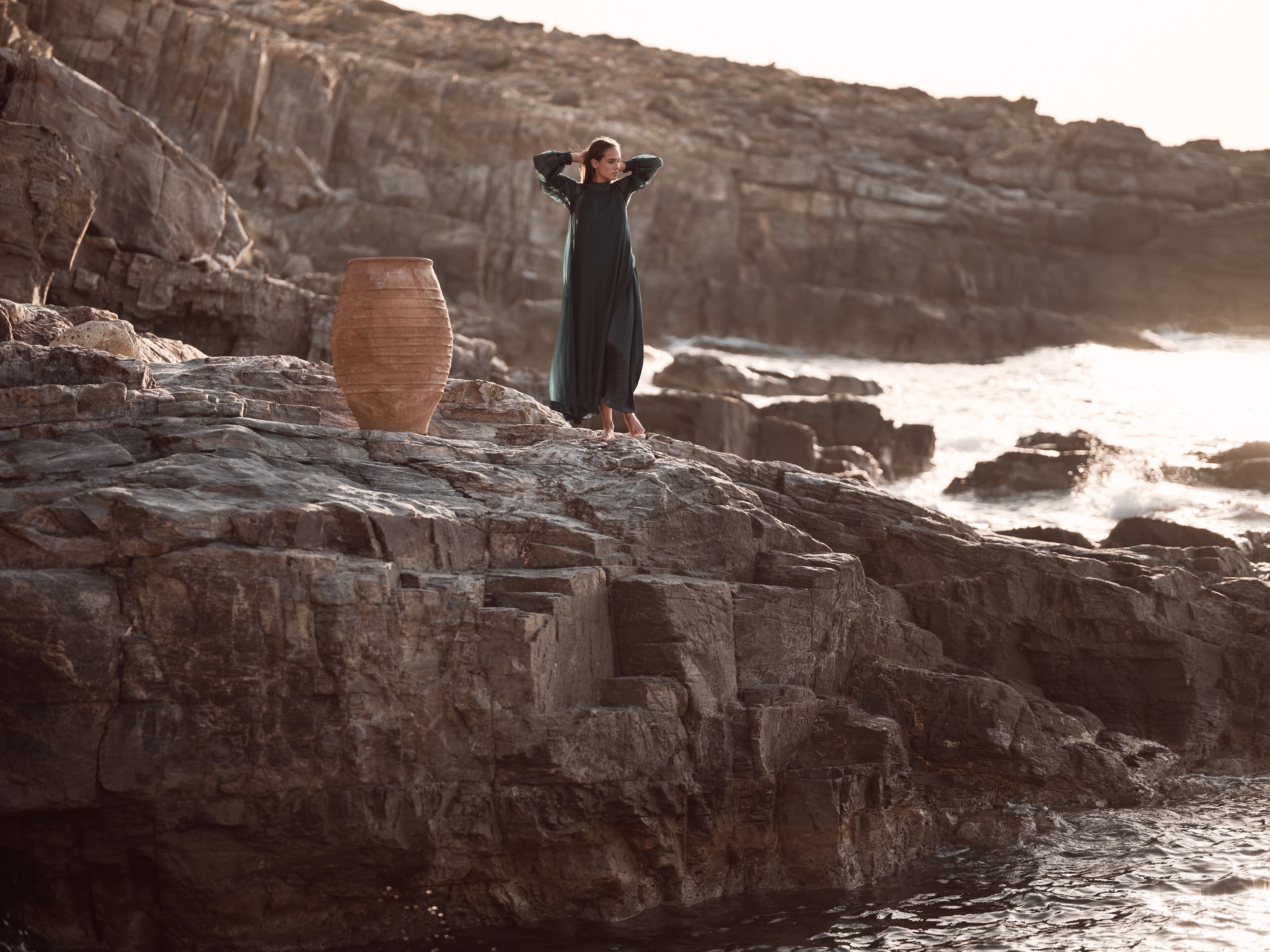 A person standing on rocky terrain with a large pot nearby.