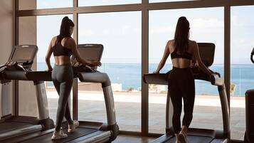 Two people using treadmills in a gym with large windows overlooking a scenic view.