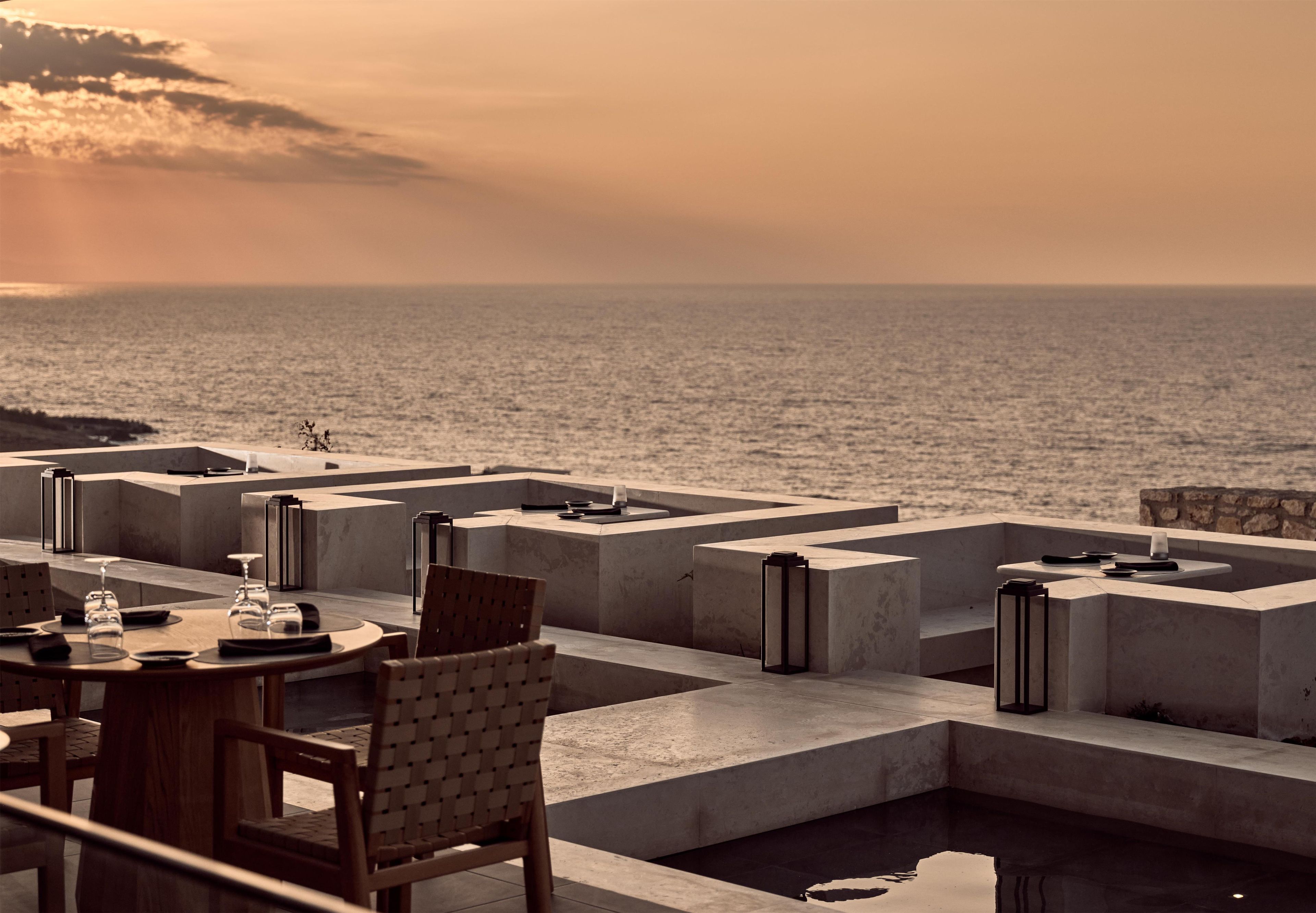 A dining area with a view of the sea, featuring a table set with glasses and plates, and a chair.