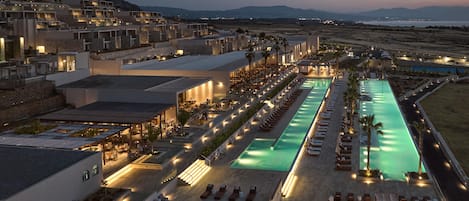 A resort with multiple swimming pools, outdoor seating areas, and a view of distant mountains.