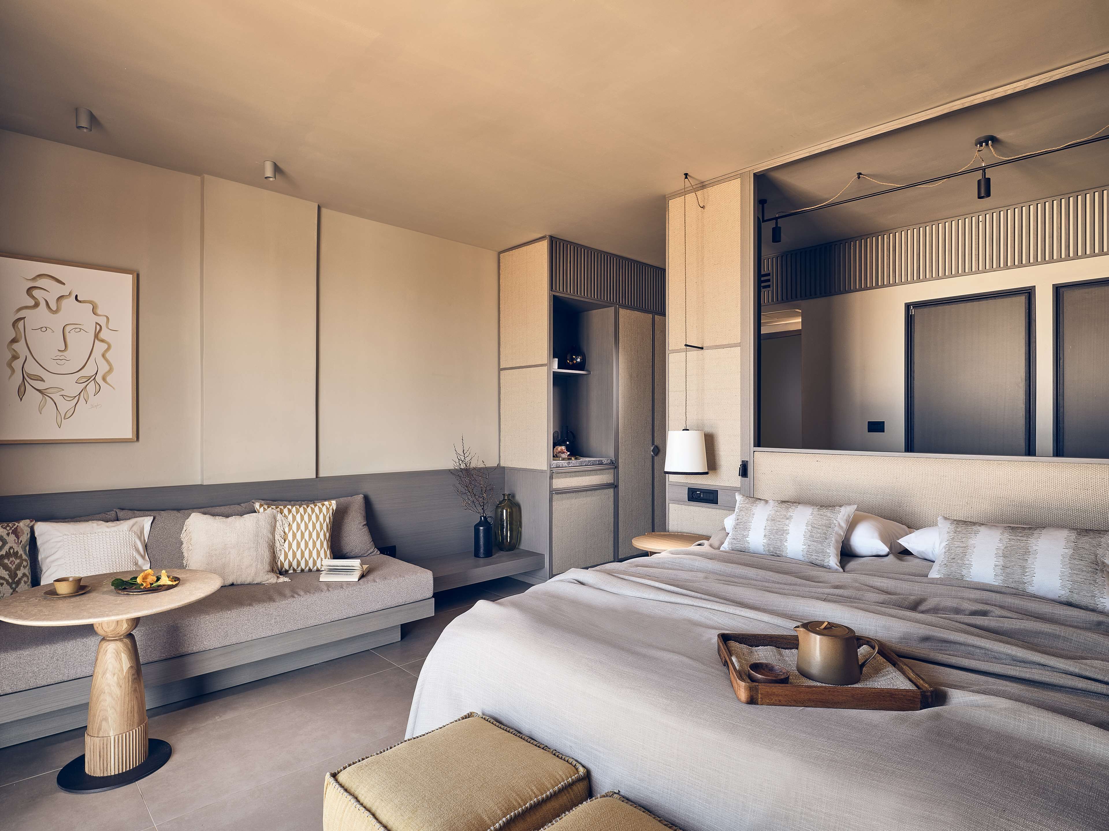 A modern hotel room with a large bed, a sofa, a small round table, and a wall-mounted TV.