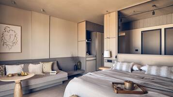 A modern hotel room with a large bed, a sofa, a small round table, and a wall-mounted TV.