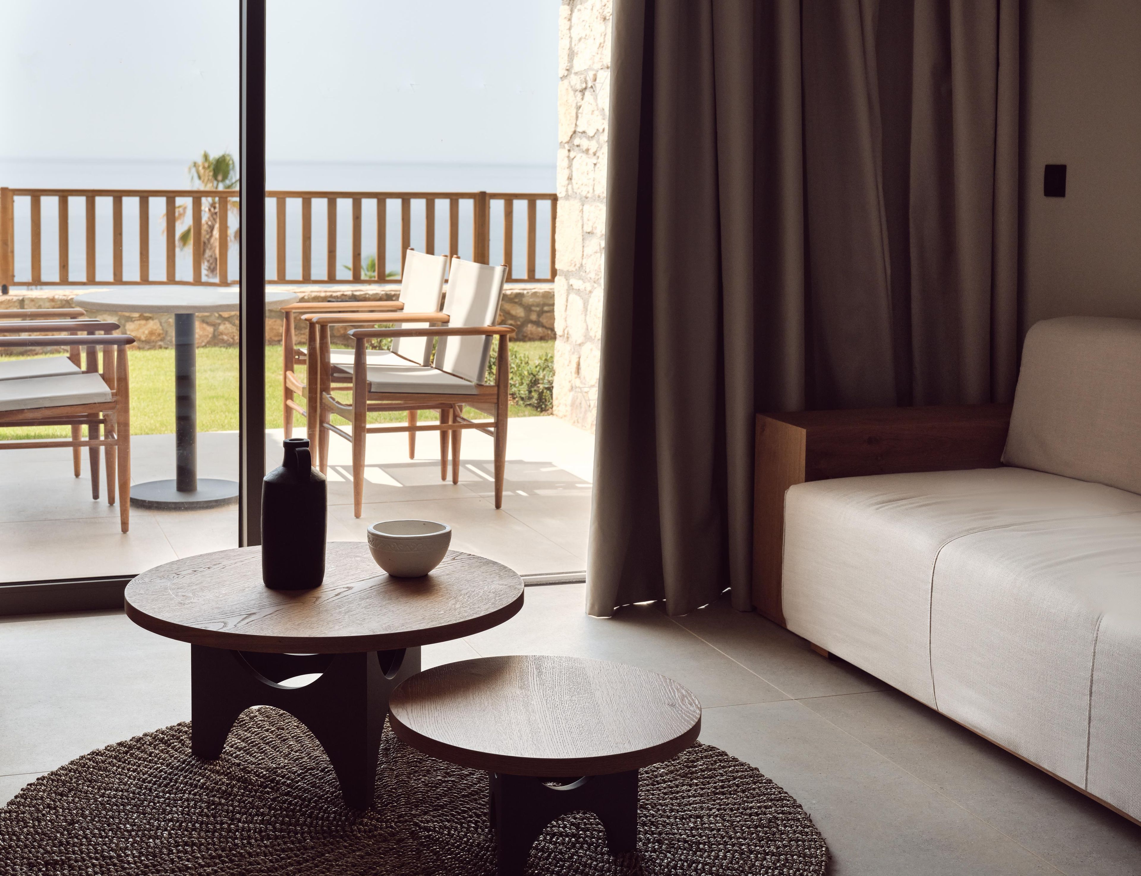 Una habitación con un sofá, una mesa con un cuenco y una botella, y vistas al exterior.