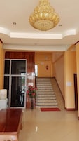 Un área de recepción con un mostrador de madera, una puerta de cristal, una escalera y una lámpara decorativa en el techo.