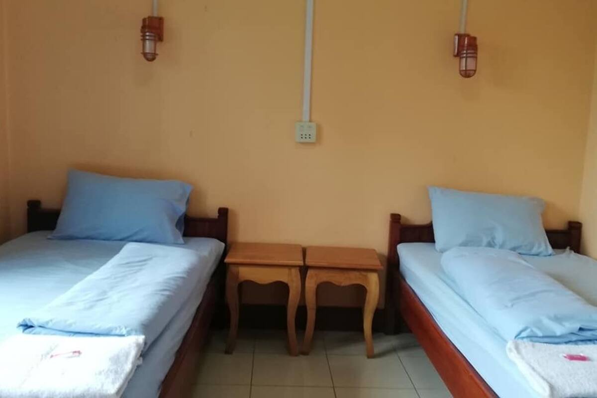 Ein Zimmer mit zwei Einzelbetten, jedes mit einem blauen Kopfkissen und einer weißen Decke. Dazwischen steht ein Holztisch.
