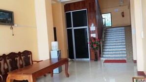 Un hall d’hôtel avec un comptoir d’accueil en bois, une grande porte vitrée, un escalier et une petite table sur laquelle est posé un vase de fleurs.