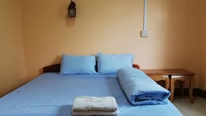 Un lit simple avec une literie bleue, une petite table de chevet et une lampe fixée au mur.