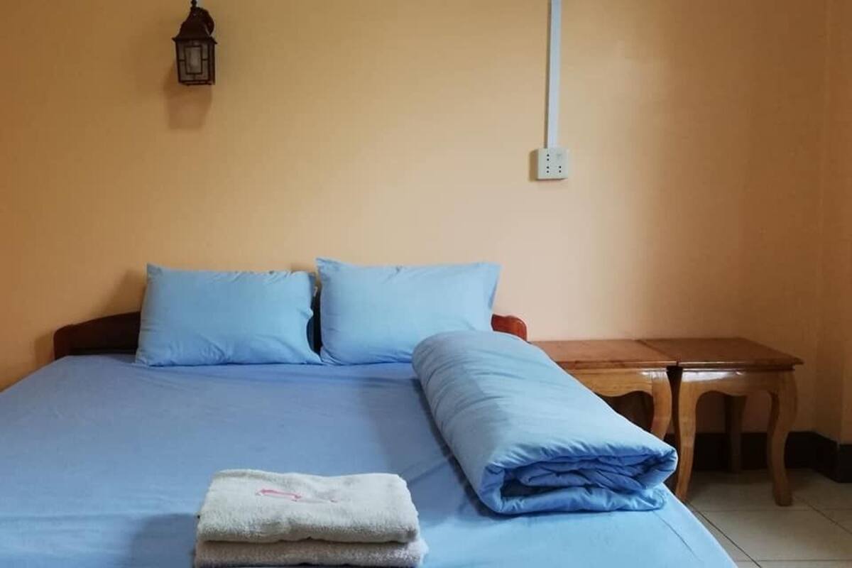 Ein Einzelbett mit blauer Bettwäsche, ein kleiner Nachttisch und eine Wandlampe.