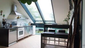 A modern kitchen with a large window, a dining area with a bench, and a view of greenery outside. - Immas Welt (Utting am Ammersee)