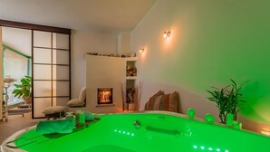 A spa room with a green-lit hot tub, a sliding shoji screen, a fireplace, and a view of the outdoors. - Immas Welt (Utting am Ammersee)