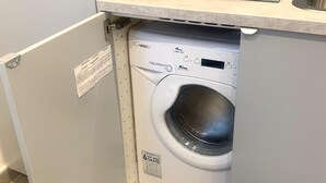 A compact, modern laundry room with a front-loading washing machine, a small countertop with a soap dispenser, and a decorative backsplash.