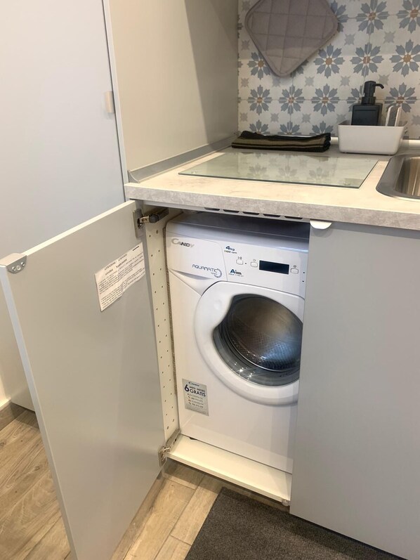 A compact, modern laundry room with a front-loading washing machine, a small countertop with a soap dispenser, and a decorative backsplash.