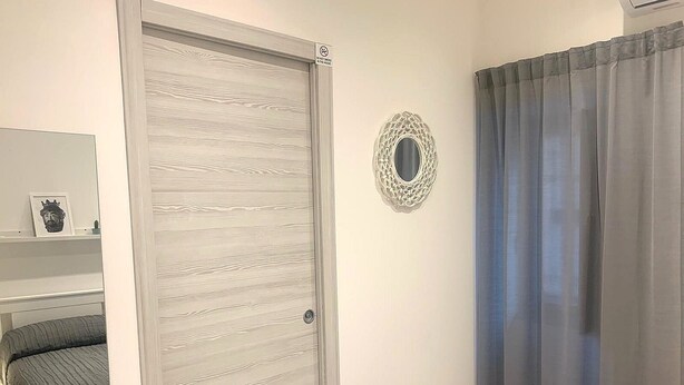 A bedroom with a sliding door, a bed, a bedside table, a mirror, and a curtain.