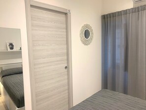 A bedroom with a sliding door, a bed, a bedside table, a mirror, and a curtain.