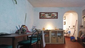 Ein Essbereich mit Holztisch und Stühlen, eine Küchenzeile mit Regalen und Kochutensilien sowie eine kleine Nische mit Beleuchtung.