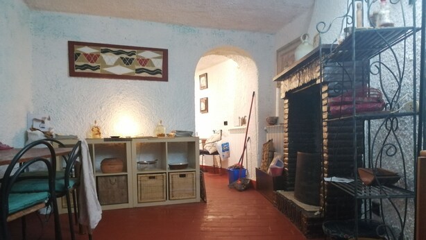 Ein Zimmer mit Holzboden, einem Tisch mit Körben, einem Regal mit Küchenutensilien und einem Wandbild.