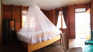 Una habitación de madera con una cama bajo un dosel blanco, paredes de madera y una silla.
