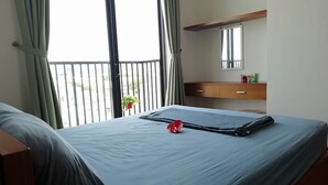 Quarto de hotel com cama, mesa de cabeceira de madeira, pequena mesa, espelho e varanda com guarda-corrimão.